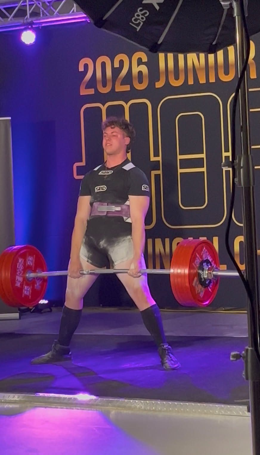Sam locking out a sumo deadlift on the platform at a 2026 junior provincial meet